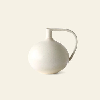 Minimalist photo of the HKLIVING Ceramic Jar M by HKLIVING—a round, off-white ceramic jar with a small spout and large curved handle, set against a plain beige background. Ideal for Mediterranean interiors and minimalist decor.