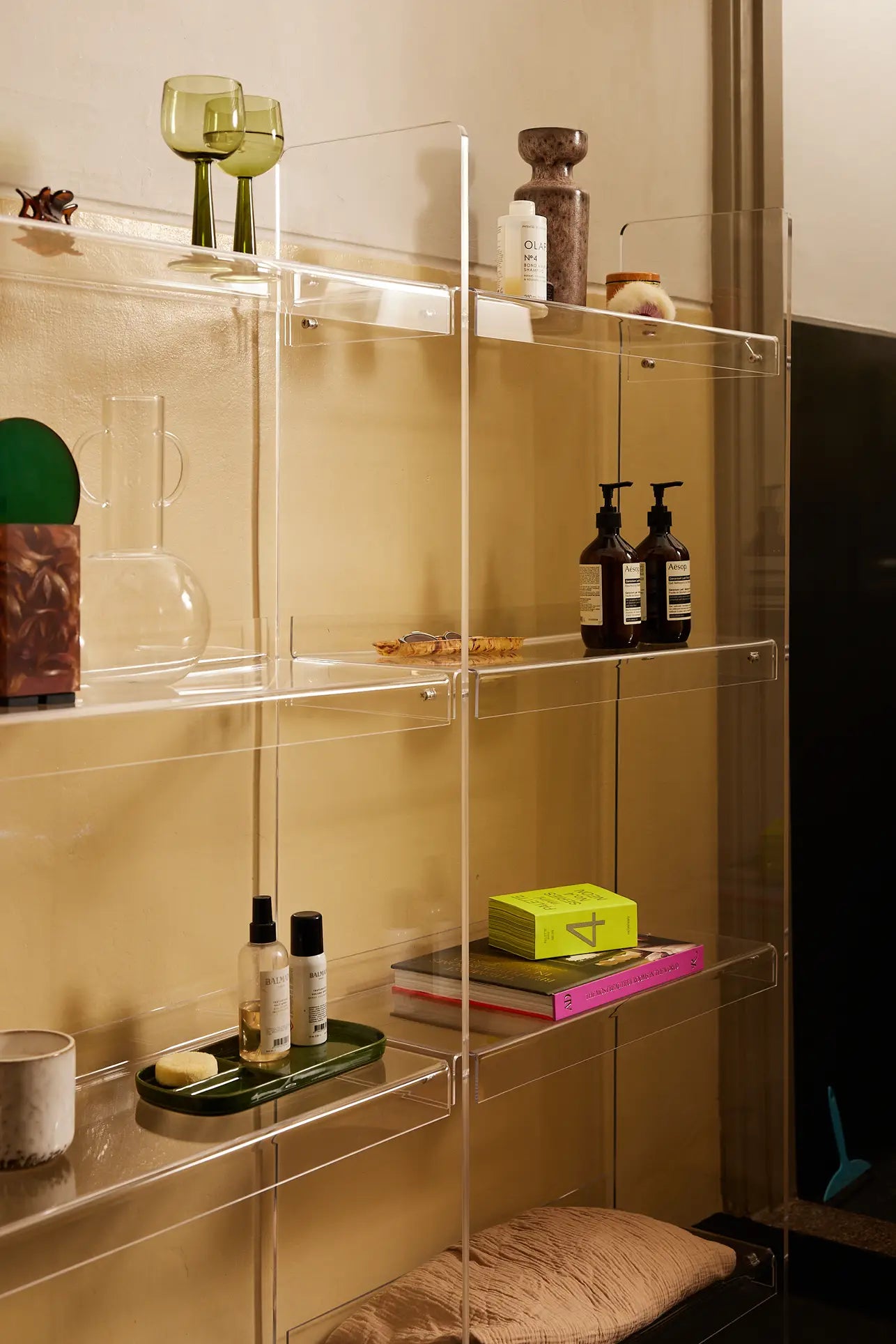 Clear acrylic shelves on a beige wall display green glasses, books, bottles, decor items, and an HKLIVING Ceramic Retro Vase in lava brown on the bottom shelf for a tidy, modern look.