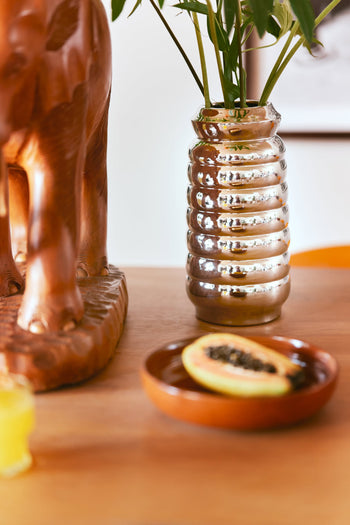 A wooden elephant sculpture stands beside the HKLIVING Ceramic Ribble Vase filled with green leaves and a brown plate holding a papaya slice on a wooden table—an elegant touch by HKLIVING for modern interiors.