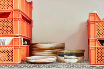 Stacked orange plastic crates and HKLIVING Chef Ceramics: Deep Plate M are arranged on a metal wire shelf against a light-colored wall.