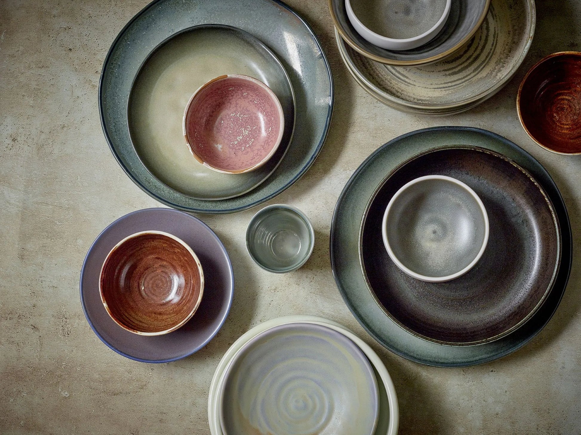 HKLIVING Chef Ceramics: Flat Bowls by HKLIVING, featuring hand-glazed finishes in muted earth tones, are artfully arranged on a textured surface. The varied sizes and glazes offer an elegant, rustic look when seen from above.