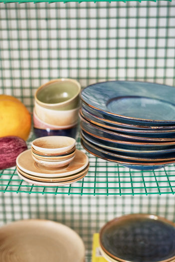 HKLIVING Chef Ceramics: Pasta Plates by HKLIVING are stacked on green wire shelving before a white and green grid wall, with a grapefruit and red onion placed beside the artisanal dishes.