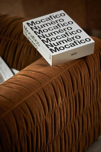 A book titled Mocaﬁco Numéro with bold black lettering on a white cover rests on the arm of the HKLIVING Club Couch, adding an elegant touch to modern interiors.