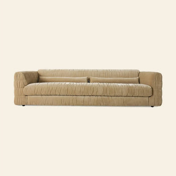 The HKLIVING Club Couch by HKLIVING features deep horizontal tufting, plush cushions, pleated beige upholstery, and low arms—showcasing a contemporary, minimalist look ideal for modern interiors. Set against a plain light background.