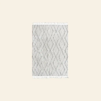 The HKLIVING Cotton Berber Rug (140x200) by HKLIVING is a rectangular, light gray rug with a subtle diamond pattern and white fringe on the short sides, shown against a plain beige background.