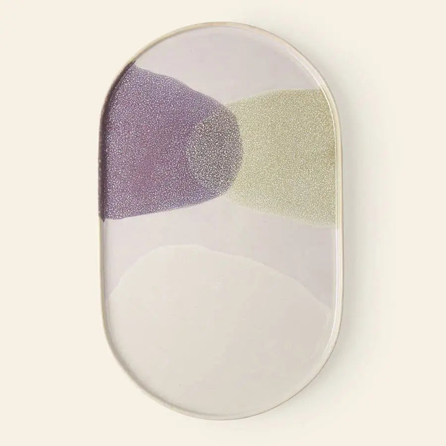 The HKliving Gallery Ceramics Oval Dinner Plate features a glossy white finish with abstract patches of lavender, pale green, and off-white overlapping at the center on a light beige background.