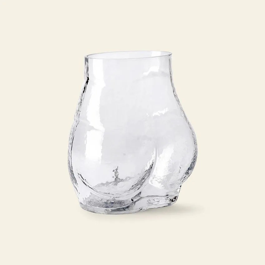 The HKLIVING Glass Bum Vase by HKLIVING adds playful charm to your decor with its cheeky, clear glass design inspired by human curves, making a unique statement on any plain light background.