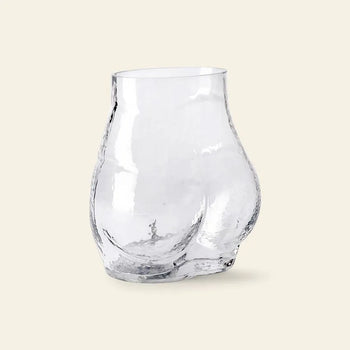 The HKLIVING Glass Bum Vase by HKLIVING adds playful charm to your decor with its cheeky, clear glass design inspired by human curves, making a unique statement on any plain light background.