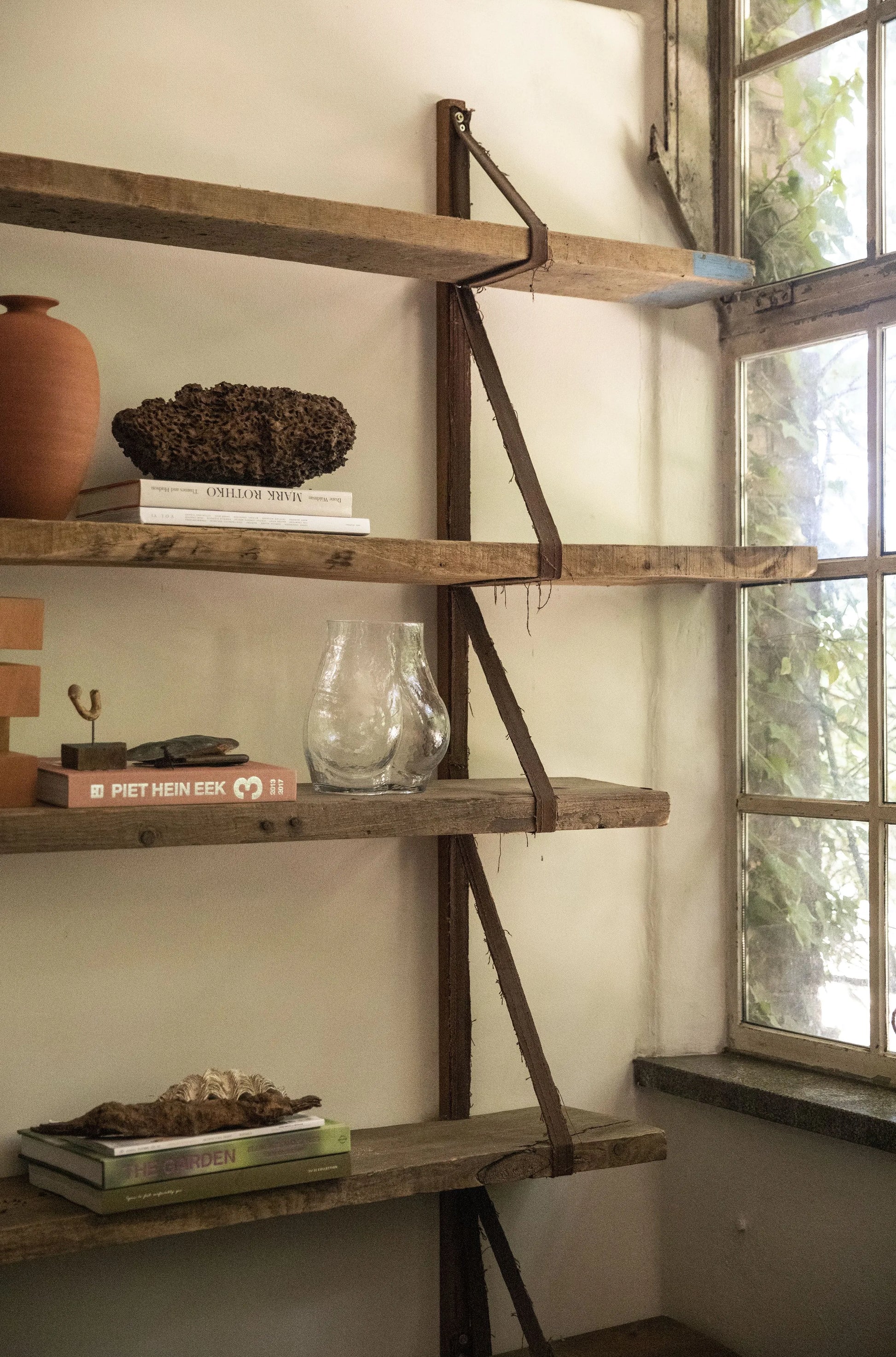 A rustic wooden bookshelf displays books, a HKLIVING Glass Bum Vase, a terracotta pot, and natural accents. Sunlight streams through a window with green leaves outside, creating a warm and peaceful ambiance.