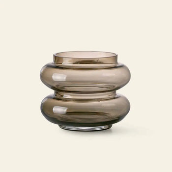 The HKliving Glass Vase S by HKliving features smoky brown, rounded glass with a wide, bulbous design and bold curves—creating a striking minimalist statement against a light beige backdrop.