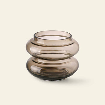 The HKliving Glass Vase S by HKliving, featuring a round, smoky brown glass design with a wide, wavy, and bulbous shape, brings minimalist elegance to your decor against a light beige backdrop.