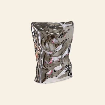 The HKLIVING HK Objects: Bag of Crisps Vase by HKLIVING features a shiny, metallic finish and sculptural, crumpled form. Its reflective surface with colorful hints makes it playful decor against any neutral background.