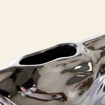 Close-up of the HKLIVING HK Objects: Bag of Crisps Vase by HKLIVING, featuring a shiny silver abstract design with a smooth, uneven surface and an irregular oval opening, perfect as playful decor against a light beige background.