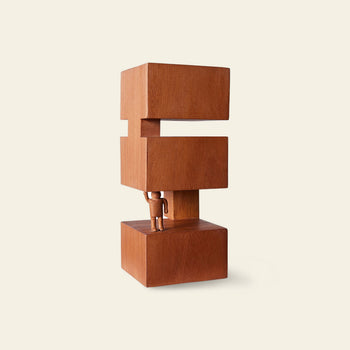 A small human figure lifts a large geometric wooden sculpture of three stacked blocks with a gap, set against a plain beige background. The HKLIVING HK Objects: Empowered by HKLIVING is perfect Bauhaus-inspired art for modern interiors.