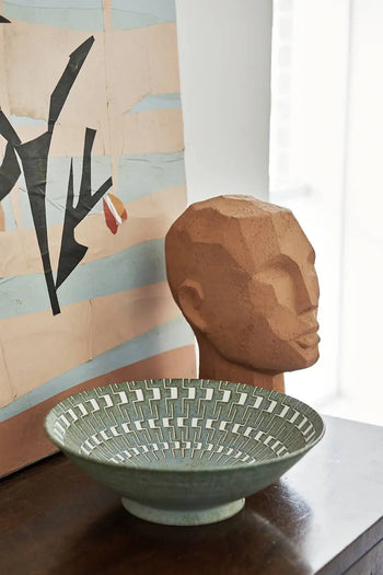 A geometric clay head sculpture sits beside a modern abstract painting and an HKLIVING Kyoto Ceramics Japanese ceramic salad bowl on a dark wooden surface.
