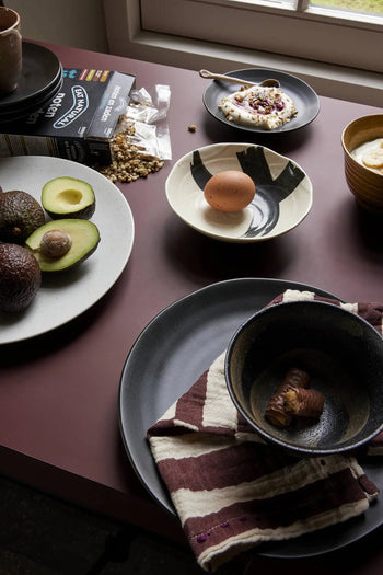 A mauve table set for breakfast features halved avocados, a brown egg in a black-and-white bowl, chestnuts, yogurt with toppings, granola, and HKLIVING Kyoto Ceramics Japanese Matcha Bowls (set of 3) beside a folded checked napkin on a plate.