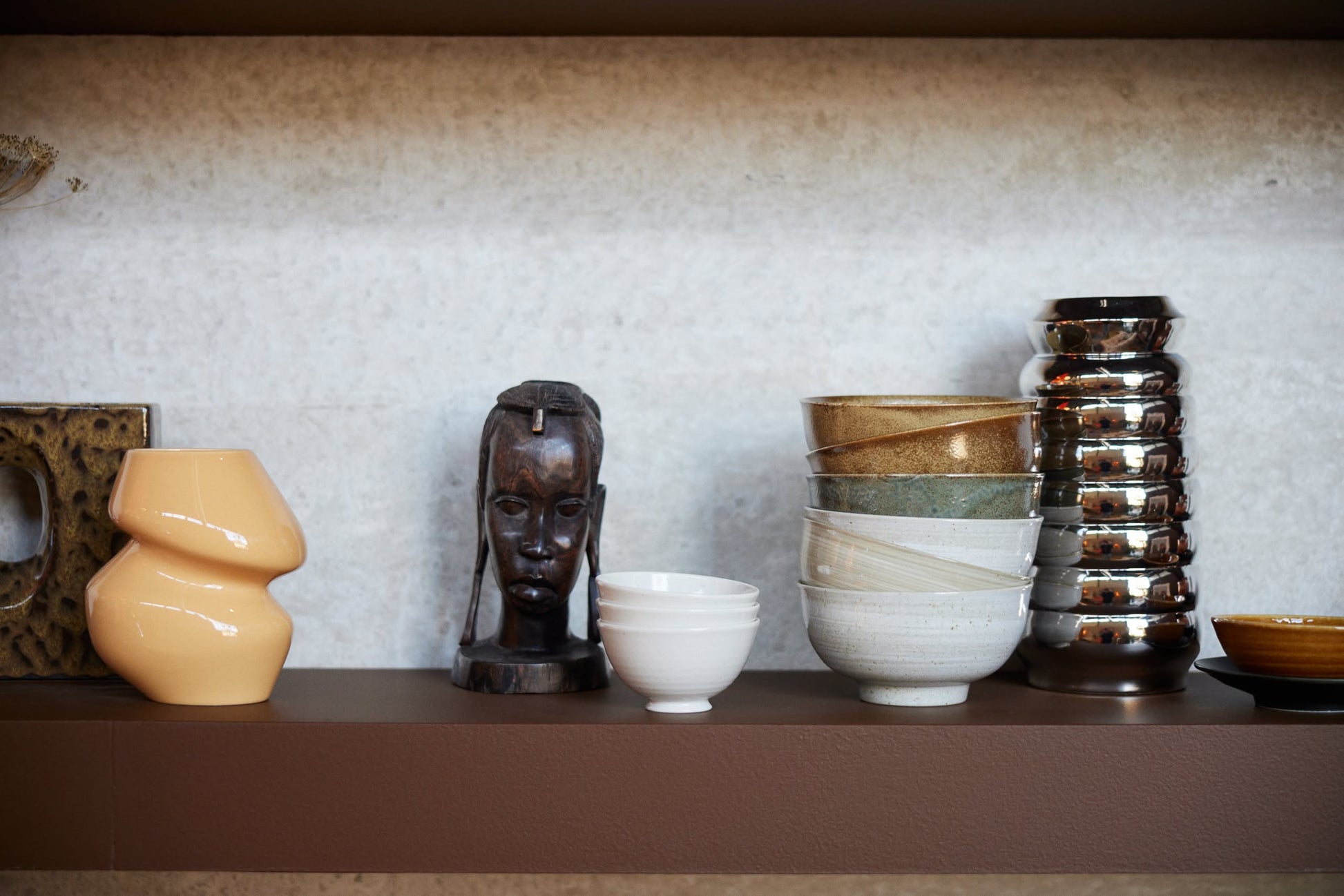 A shelf displays a beige abstract vase, a carved wooden head sculpture, shiny metallic cups, a small brown dish, and HKLIVING Kyoto Ceramics Japanese Noodle Bowls (Set of 4), all set against a neutral background.