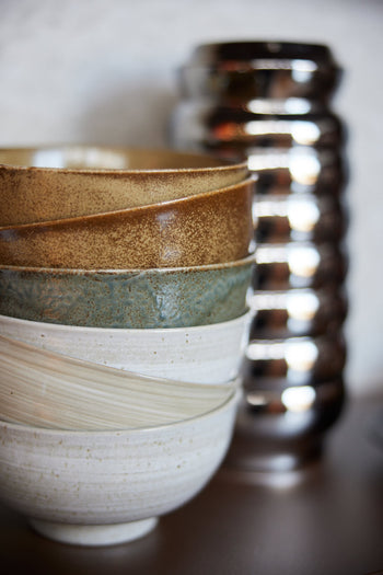A close-up of HKLIVING Kyoto Ceramics Japanese Noodle Bowls, set of 4, hand-finished in earthy tones and textures, stacked near a metallic ribbed vase.