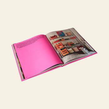 The HKLIVING Limited Edition Lookbook '22 by HKLIVING is displayed open on a cream background, featuring a bright pink left page with text and a right page showing a vibrant, colorful room for bold visual inspiration.