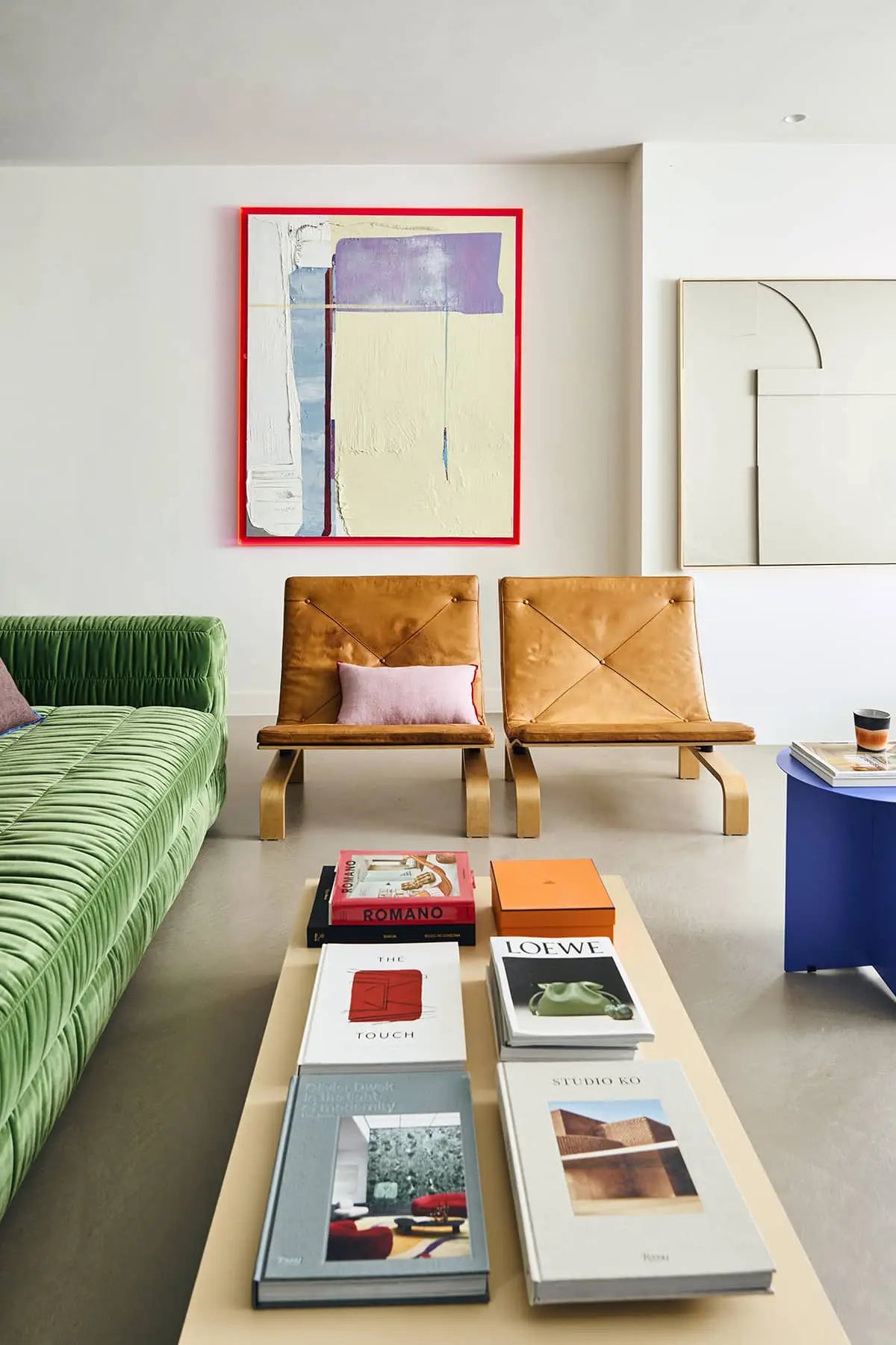 A modern living room featuring a green sofa, two tan leather chairs, a beige coffee table with art books, the HKLIVING Metal Side Table Round by HKLIVING with a cup, and abstract art on white walls.
