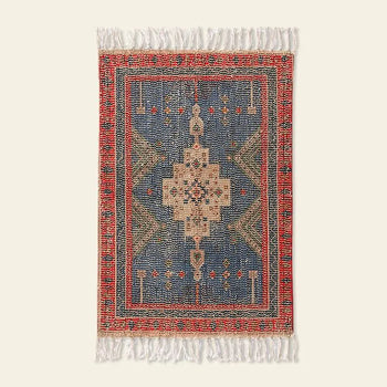 The HKLIVING Printed Bathmat Overtufted by HKLIVING is a rectangular mat with an intricate geometric pattern in blue, red, beige, and green, a central medallion, white fringe on short edges, and an anti-slip backing for safety.