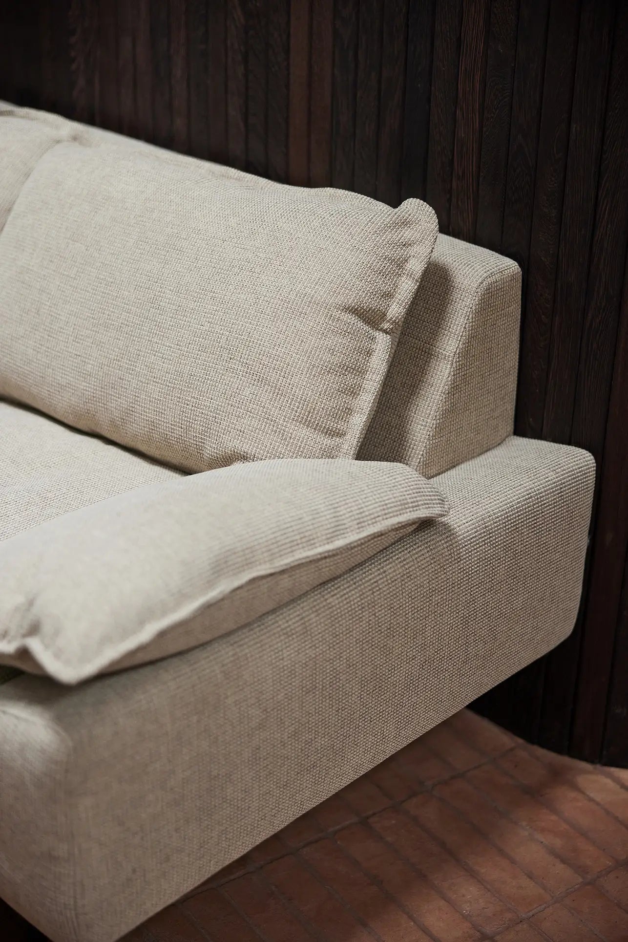 A close-up of the HKLIVING Retro Sofa, 2-Seats in beige with plush cushions, by HKLIVING, set against a dark wooden wall and reddish-brown tiled floor.