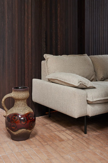 The HKLIVING Retro Sofa, 3-Seats by HKLIVING sits on a light wood floor next to a large brown ceramic jug-style vase with circular patterns, set against vertical dark wood paneling.