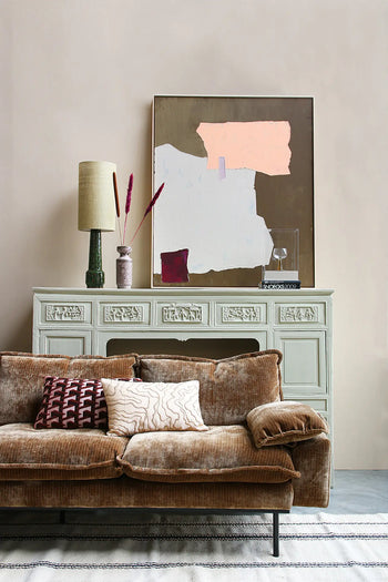 A cozy living room featuring the HKLIVING Retro Sofa, 4-Seats by HKLIVING with patterned pillows, a light green vintage console table behind it, modern abstract art, a lamp, vase with dried flowers, and decorative accents on the table.