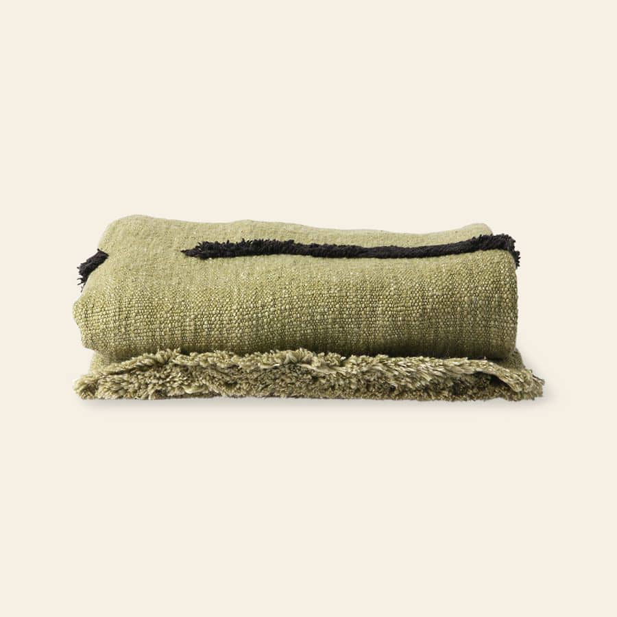 The HKliving Soft Woven Throw With Black Tufted Lines, a cosy olive green cotton throw with stylish texture and fringed edges, is displayed on a light beige background.