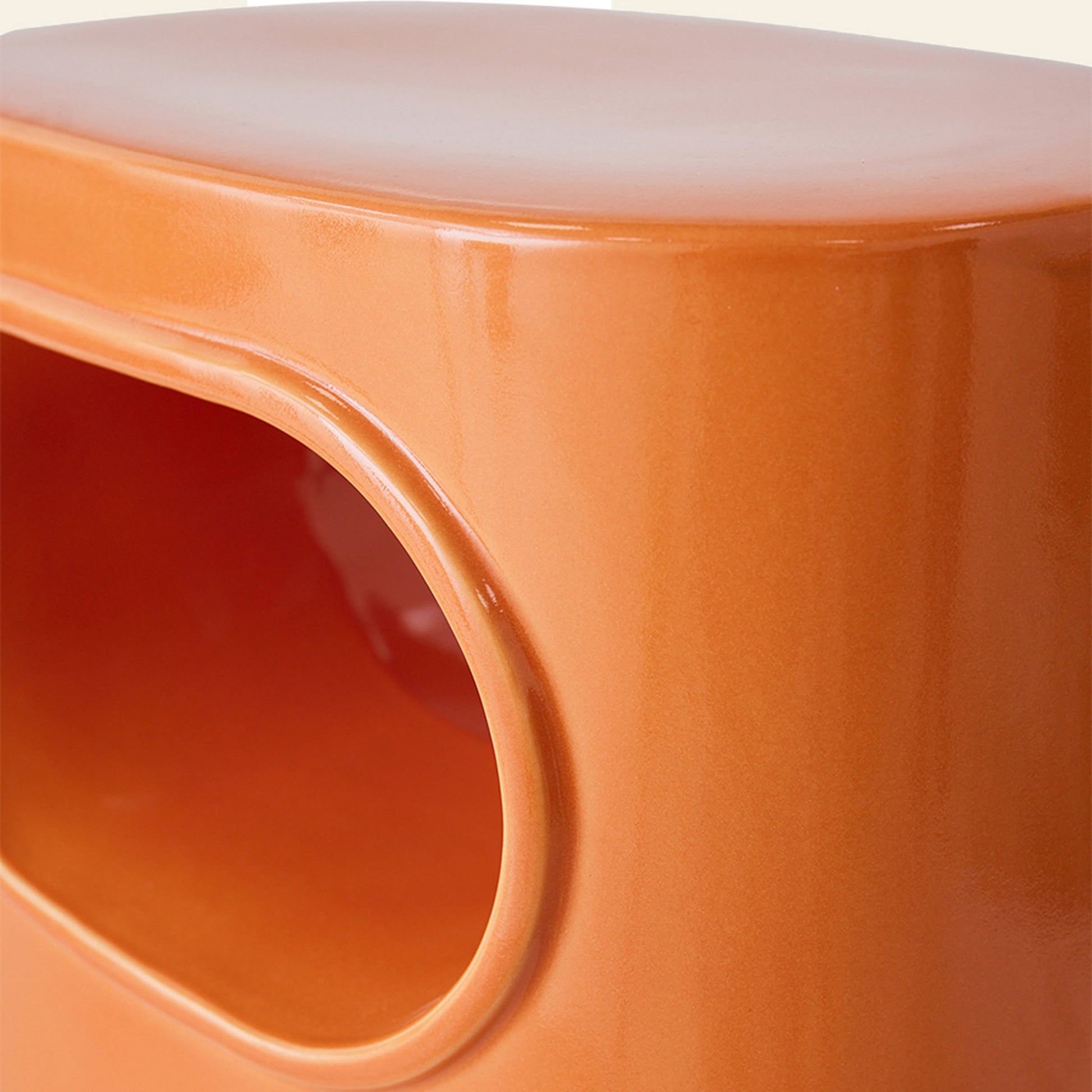 Close-up of the HKLIVING Space Side Table by HKLIVING, featuring glossy orange ceramic, a rounded rectangular silhouette, and an oval cut-out for storage. Its sleek, light-reflecting surface makes it ideal for modern interiors.