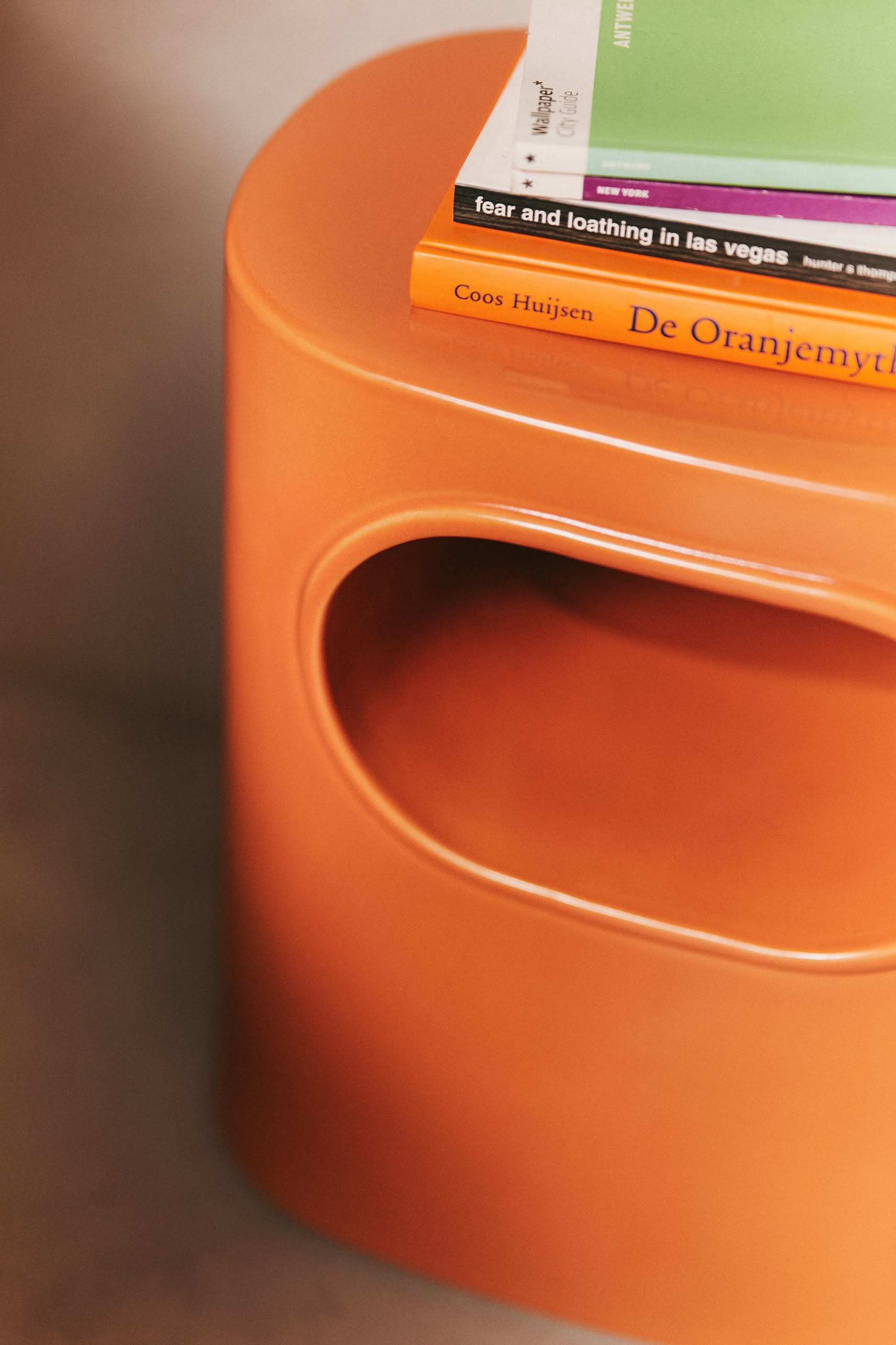 Close-up of the HKLIVING Space Side Table by HKLIVING, featuring a rounded cutout, built-in storage, and topped with books including Fear and Loathing in Las Vegas and De Oranjemythe by Coos Huijsen.