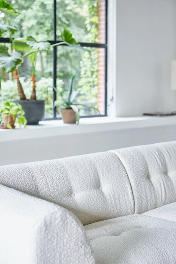 The HKLIVING Vint Couch, Left, 1.5-Seat by HKLIVING features roomy white textured fabric and sits before a sunlit window with green potted plants, highlighting the lush greenery outside.