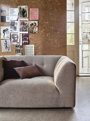 The HKLIVING Vint Couch Loveseat by HKLIVING, with two cushions, sits before a cork wall filled with photos and notes. A glass-panel door lets in natural light, enhancing the room’s stylish and cozy vibe.