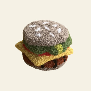 The Habichl Burger Coasters Set by Habichl features handmade crocheted coasters resembling a burger with a sesame seed bun, lettuce, tomato, cheese, and patty. Perfect for adding fun to your table. Plain beige background.