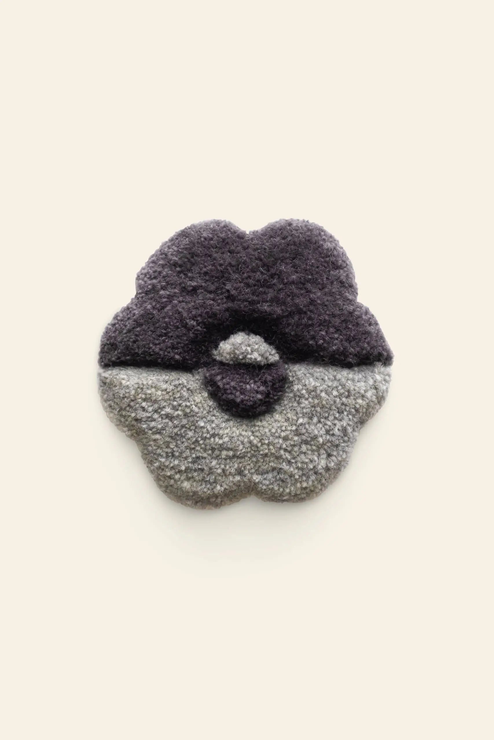 A textured, abstract flower-shaped rug in dark purple and light gray, inspired by the exclusive Habichl Tufted Coasters and Handmade Wooly Flower Coasters. Features a unique tufted design on an off-white background. Brand: Habichl.