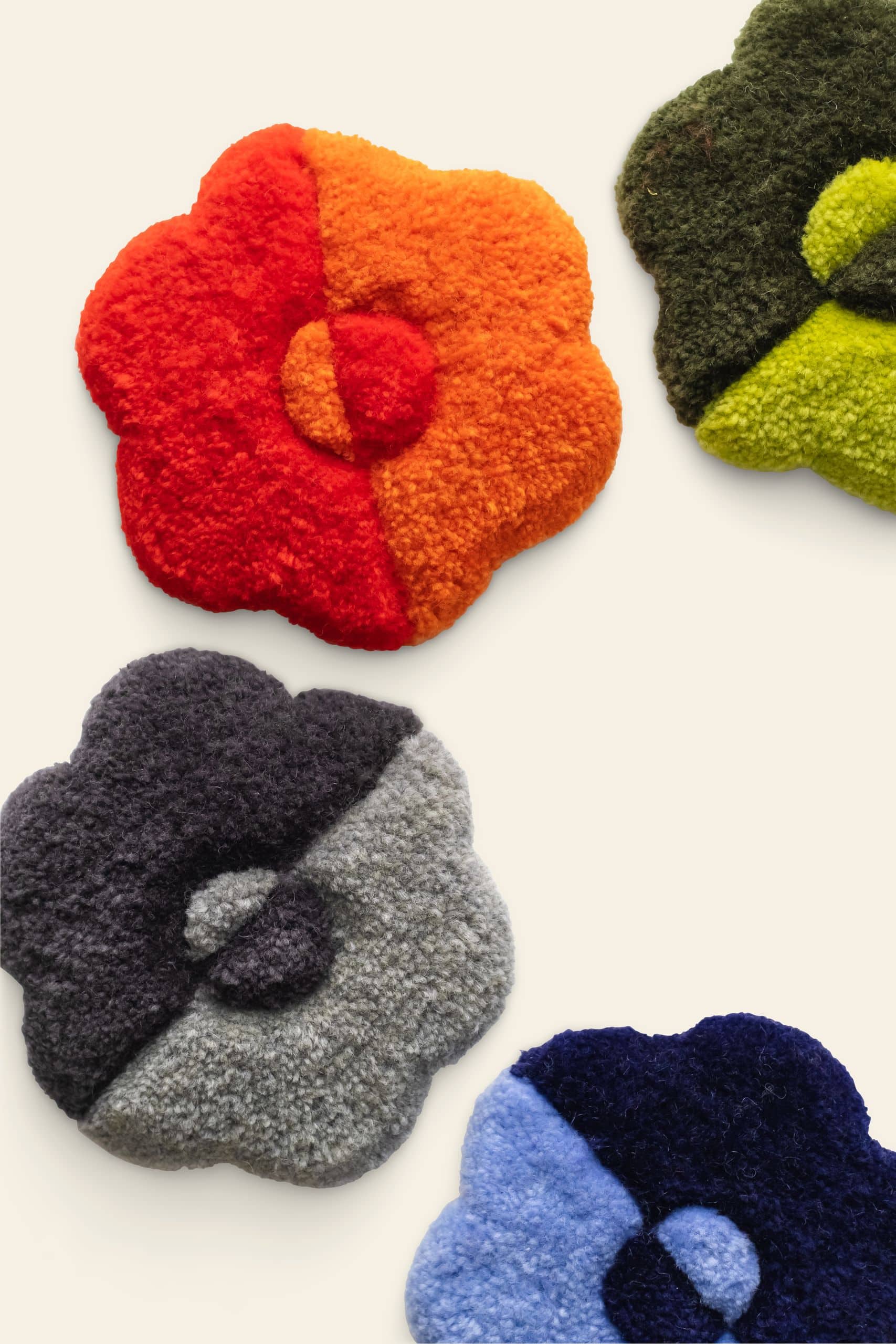 Habichl Tufted Coasters by Habichl—set of four, each with a unique tufted design in red & orange, green & yellow, gray & black, and blue & navy—are displayed on a light background.