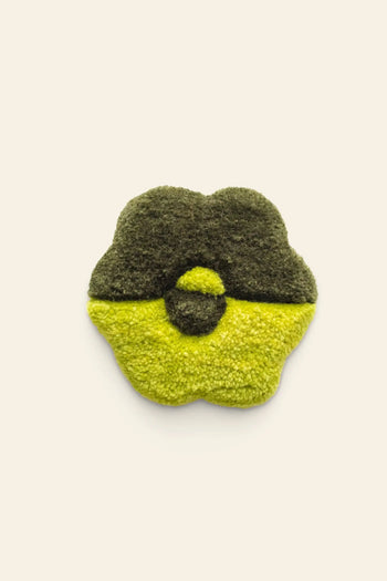 A green and yellow flower-shaped patch with a unique tufted design by Habichl, inspired by the Habichl Tufted Coasters, is displayed on a plain beige background.