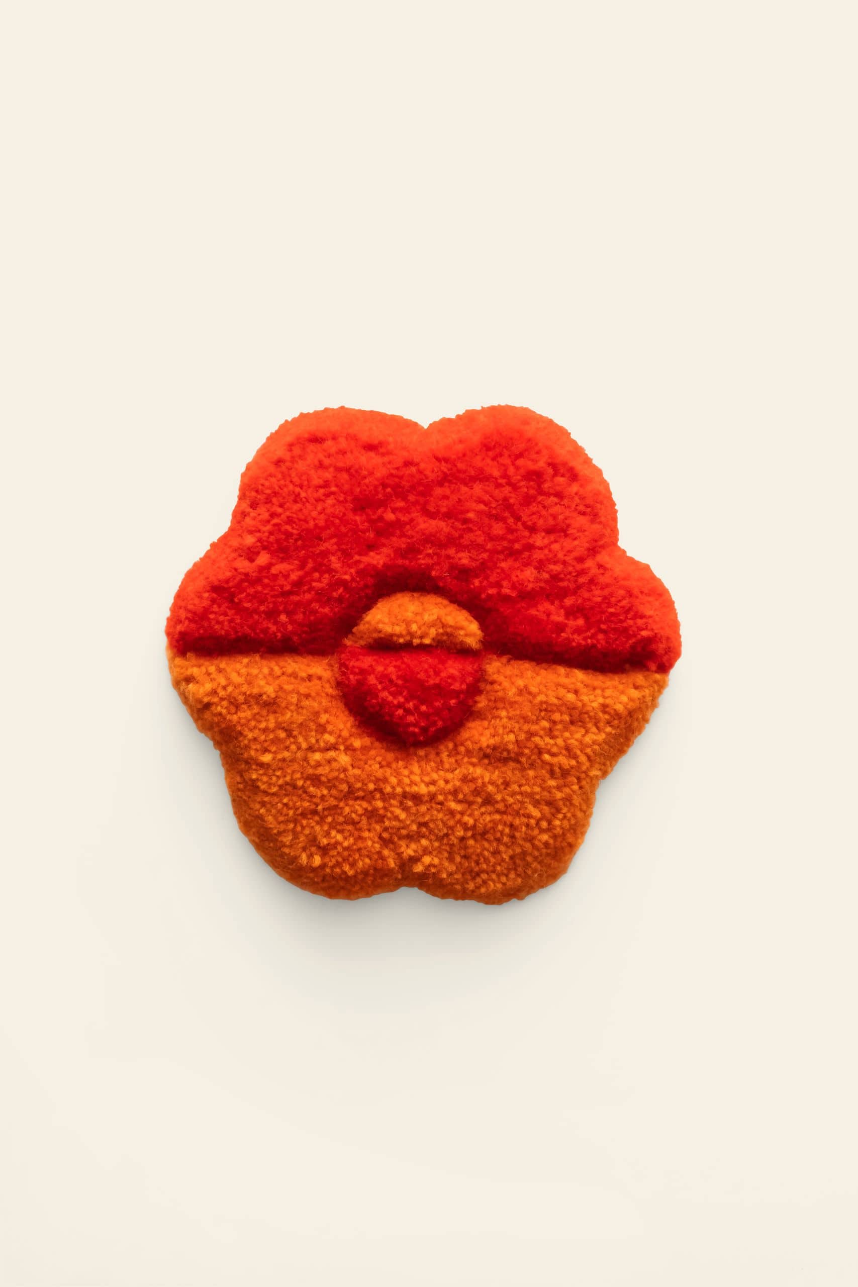 A handmade Habichl Tufted Coaster by Habichl, featuring a flower shape with a unique tufted design and fluffy texture, red on top and orange on the bottom, is showcased against a plain off-white background.