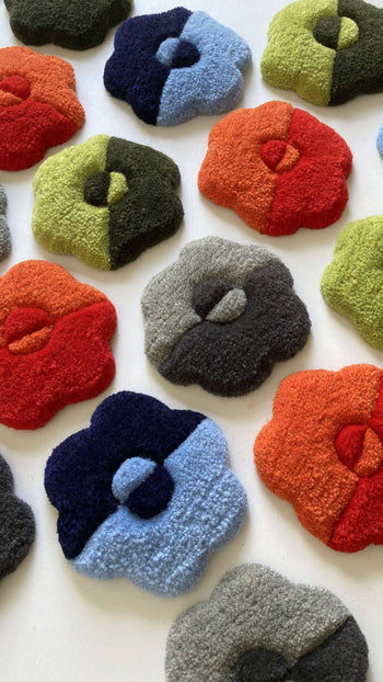 Habichl Tufted Coasters by Habichl, featuring a unique textured design, are displayed on a white surface. Each flower-shaped coaster pairs two contrasting colors such as blue, green, red, orange, black, and gray.