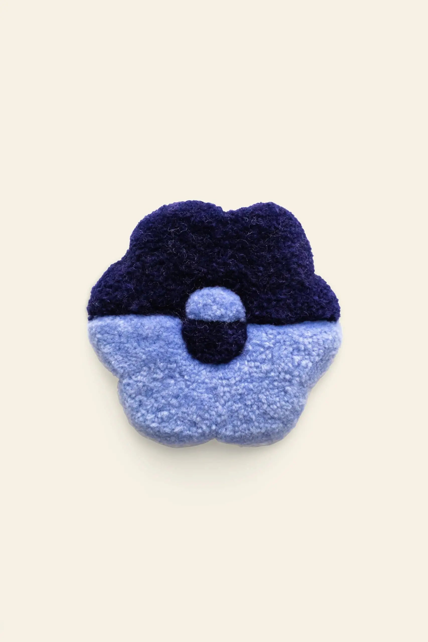 The Habichl Tufted Coasters by Habichl are plush, flower-shaped coasters with a unique tufted design—dark blue petals on top, light blue below, and a dark blue center—set against a plain beige background.