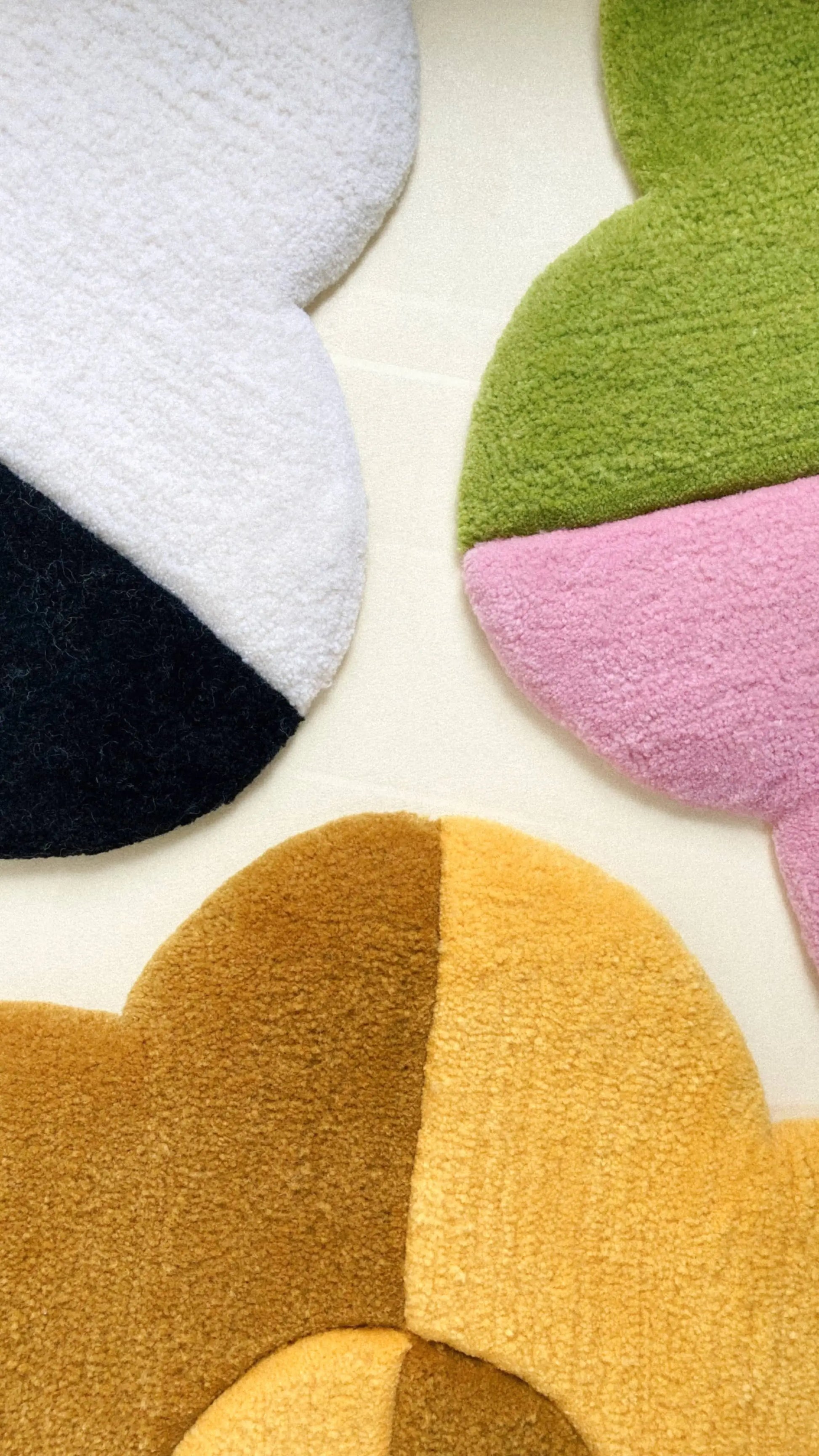 The Habichl Tufted Flower Floor Rugs by Habichl—three abstract, flower-shaped rugs in white/black, green/pink, and yellow/brown color blocks—add whimsy and charm when arranged on a light surface.