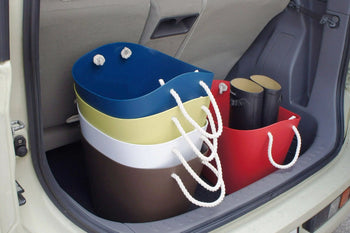 Four vibrant Hachiman Balcolore Storage Basket M bins with rope handles and two rolled-up mats are neatly arranged in a car trunk. The Japanese-designed baskets are nested together, with the mats stored inside a red basket for versatile use.
