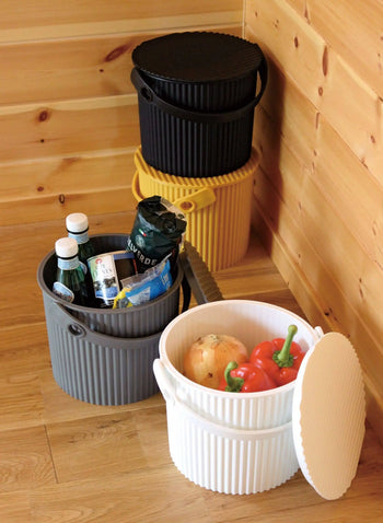 Four ribbed plastic storage bins, including the Hachiman Omnioutil Storage Bucket S, are stacked in a wooden room corner. The gray and white Hachiman bins are open, holding groceries and vegetables—ideal for indoor or outdoor use.