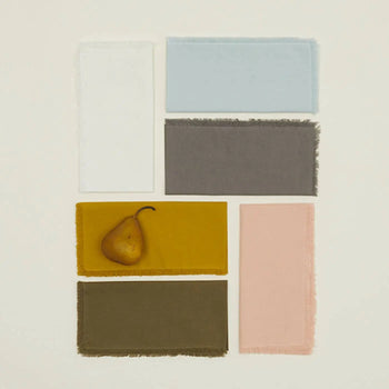 Four rectangular fabric swatches in white, light blue, gray, and mustard yellow are displayed—highlighting the stylish Hawkins New York Essential Dinner Napkins, Set Of 4 by Hawkins New York, ideal for elevating any table setting.