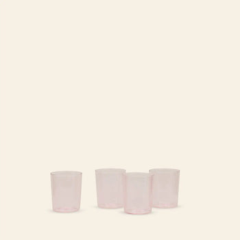 A set of four translucent pink Hawkins New York Essential Glassware (Medium) is arranged in a row on a light beige background—three grouped, one set apart—showcasing the brand’s premium quality.