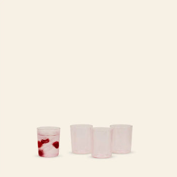 Four translucent pink Hawkins New York Essential Glassware, Set Of 4, Medium are displayed on a plain background—three empty and one filled with ice and two red cherries—highlighting their premium quality for any occasion.