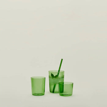 Three Hawkins New York Essential Glassware (Set Of 4, Small) green transparent glasses are on a light background; one holds ice, mint leaves, water, and a green straw while the other two are empty. Brand: Hawkins New York.