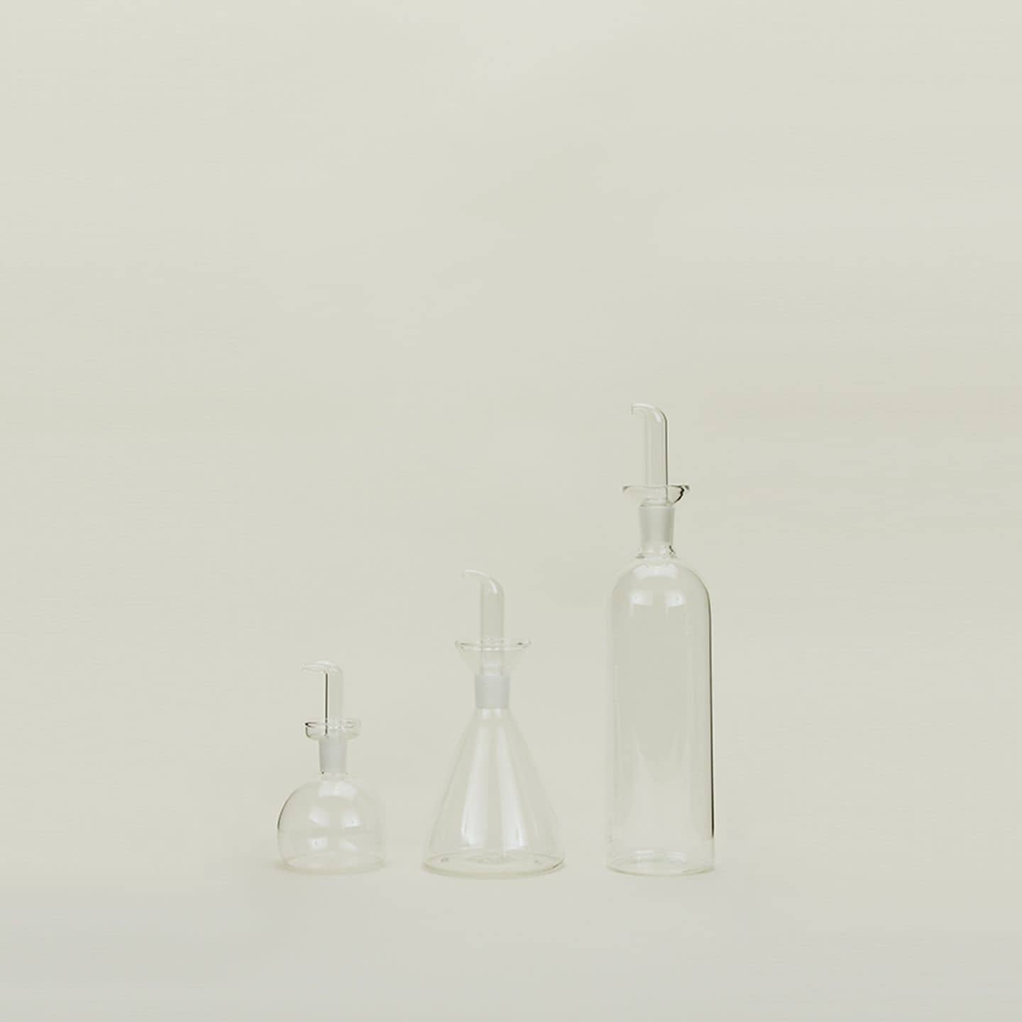 A Hawkins New York Essential Kitchen Bottle (Medium) stands against a light background, showcasing its transparent design, modern styling, and precision drizzle spout with stopper.