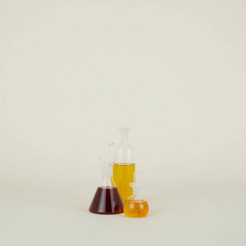 The Hawkins New York Essential Kitchen Bottles, Medium, feature modern shapes and curved glass stoppers, filled with dark red, golden yellow, and amber hues for a sophisticated countertop accent.