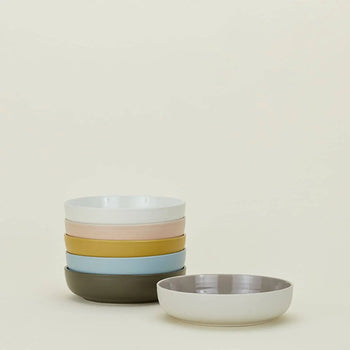 A set of four Hawkins New York Essential Low Bowls in pastel hues, with an additional matching bowl in front, adds a refined touch to your dining setting against a simple light background.